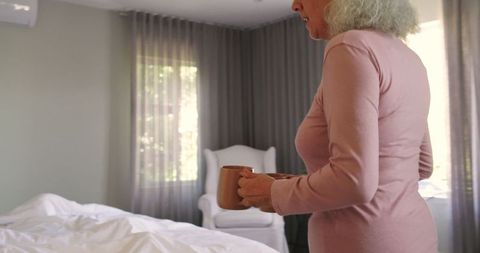 Senior woman in cozy bedroom holding ceramic mug