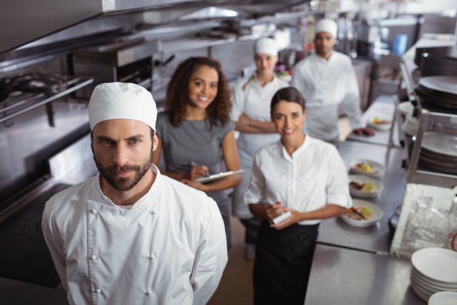 Restaurant manager standing confidently with his kitchen staff in a commercial kitchen. Ideal for use in articles about restaurant management, teamwork in the culinary industry, professional kitchen environments, and hospitality training materials.