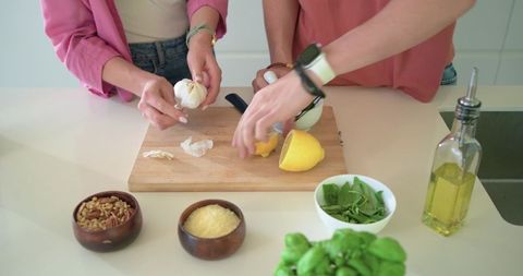 Teen couple preparing fresh basil pesto with garlic, lemon and olive oil on counter