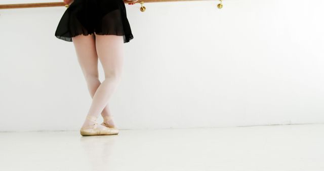 Ballerina standing in a ballet studio, practicing near a barre while wearing pointe shoes and ballet skirt. Ideal for use in content about ballet, dance training, practicing dance, fitness routines, or arts and performance.