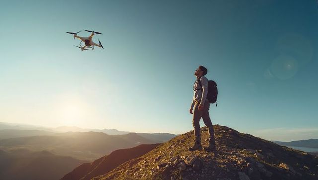 Hiking man operating drone over mountain ridge during golden hour, summit adventure