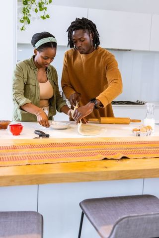 African american couple baking together on modern kitchen island, rolling pastry dough
