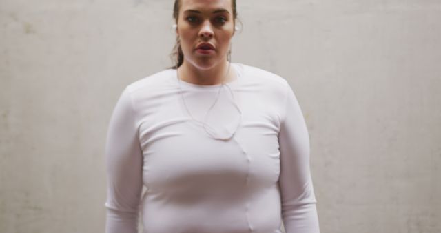 Confident plus-size woman standing against a white wall inside. She is looking forward with determination. Ideal for concepts related to body positivity, wellness, confidence, plus-size fashion, and self-assurance. Useful for lifestyle blogs, wellness programs, and fashion advertisements targeting diverse audiences.