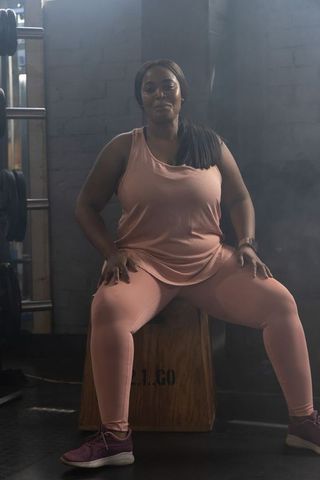 Confident african american woman sitting on plyo box in gym wearing pink activewear