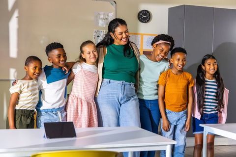 Female teacher guiding diverse elementary students smiling and bonding in bright classroom