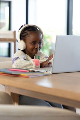African american girl learning online with headphones and laptop, focused home study