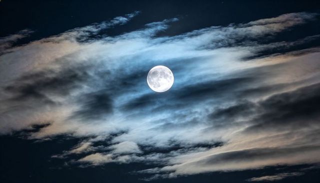Full Moon Shining Through Layered Clouds with Silvery Halo Over Deep Night Sky Landscape