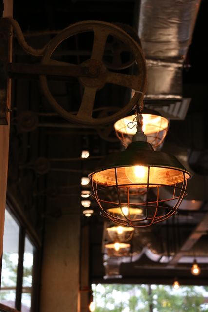 Vintage industrial hanging light fixtures illuminating interior of modern café. Metal and rustic elements combined with warm light create cozy atmosphere. Ideal for use in design projects showcasing industrial styles, modern interiors, café decor, or rustic themes. Suitable for architectural presentations, interior design charters, restaurant promotion, and lifestyle blogs highlighting unique decor.