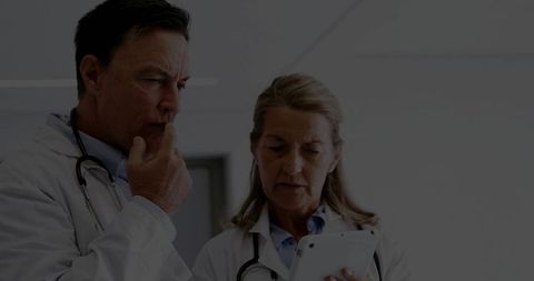 Two clinicians consulting over tablet in hospital corridor reviewing patient records