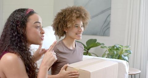 Friends unboxing delivery box on bright modern sofa, smiling and enjoying home moment