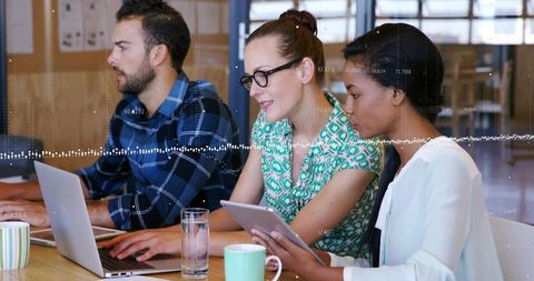 Diverse team collaborating on tablet and laptop with rising data charts overlay