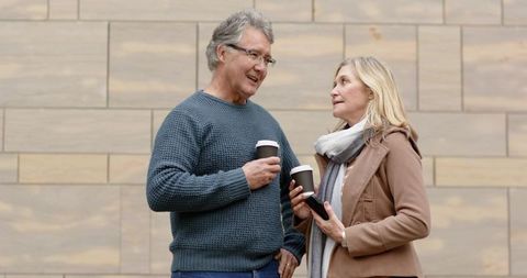 Mature couple enjoying coffee and casual conversation outdoors near urban sandstone wall