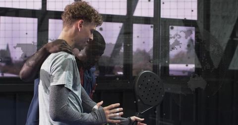 Young athletes inspecting paddle on glass court with dotted world map overlay