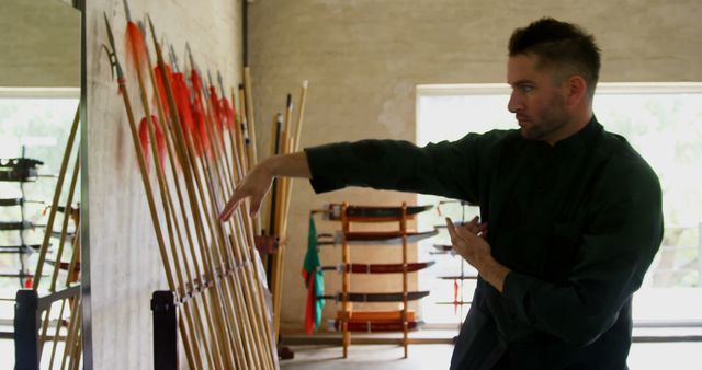 Caucasian man selects a bow in an archery range. He's focused on choosing the right equipment for his archery practice.