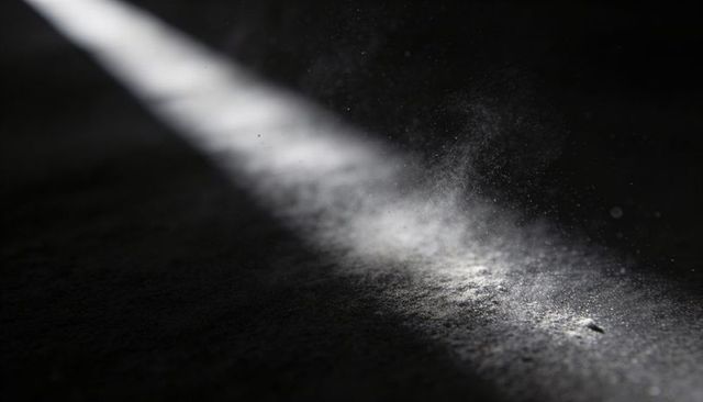 Diagonal shaft of light cutting through attic floor revealing dust motes and cracked wood
