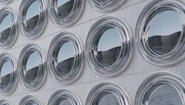 Chrome porthole window facade reflecting sky repeating circular geometric pattern