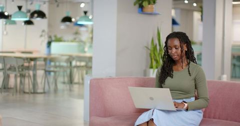 African American Woman Working on Laptop in Modern Coworking Lounge with Blush Sofa