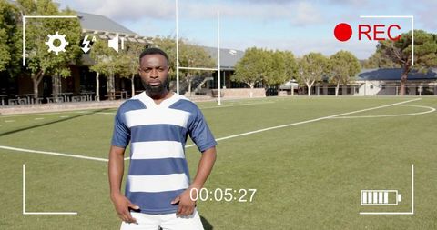 Rugby player standing on turf pitch facing camera with rec overlay and goalposts
