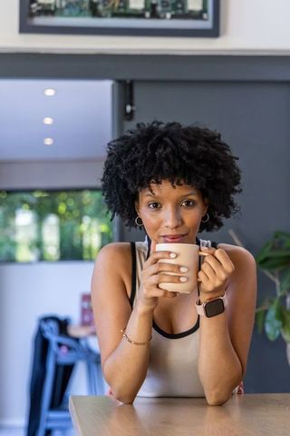 Woman leaning on kitchen counter sipping coffee while wearing pink smartwatch in cozy modern kitchen