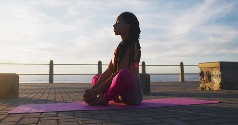 Woman Practicing Butterfly Pose on Oceanfront Promenade at Sunrise