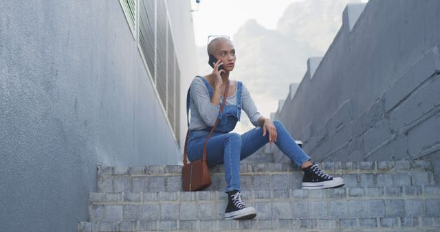 Biracial woman sitting on stairs and talking on smartphone. Street style, communication and modern urban lifestyle.