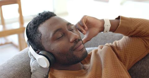 Relaxing african american man reclining on sofa listening to headphones in living room