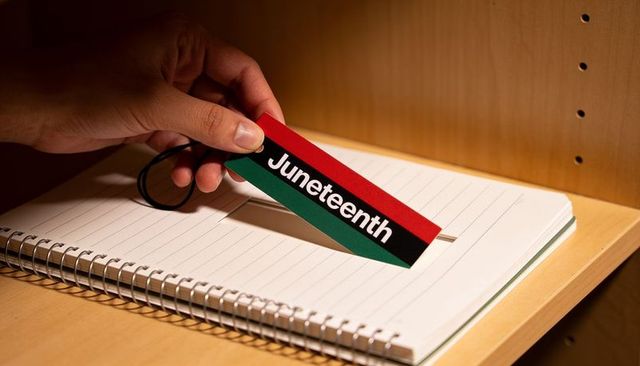Hand placing juneteenth bookmark into spiral notebook on light wooden shelf