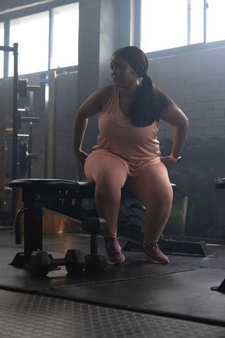 African american woman resting on weight bench in industrial gym holding dumbbell