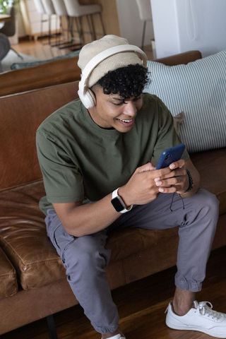 African american man lounging on couch wearing headphones streaming music from smartphone