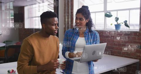 Young professionals collaborating over laptop in modern loft office with social media overlays