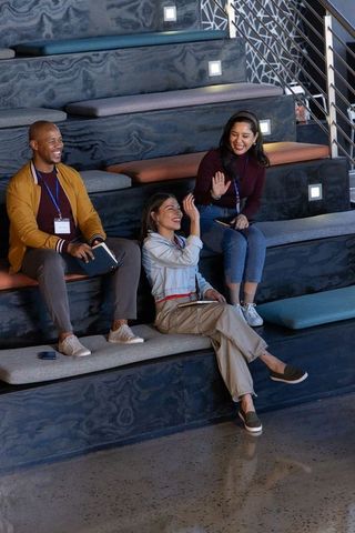 Multicultural team laughing and collaborating on tiered bench seating at coworking workshop