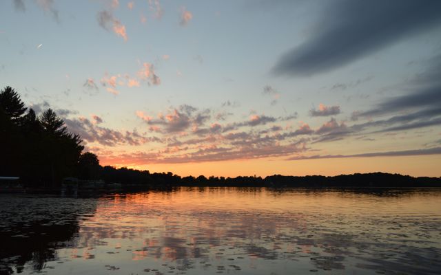 Capturing a tranquil lake at sunset with vibrant colors reflecting on the water and scattered clouds in the sky. Ideal for nature enthusiasts, relaxation-themed projects, or posters promoting peace and calmness.