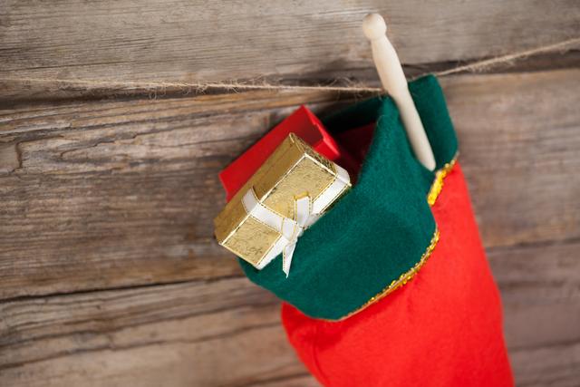 Christmas stocking filled with a golden present hanging against a rustic wooden wall. Ideal for holiday greeting cards, festive advertisements, or seasonal blog posts. Perfect for promoting Christmas sales, decorations, and holiday traditions.