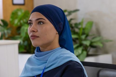 Young professional woman wearing blue hijab working in modern office with plants