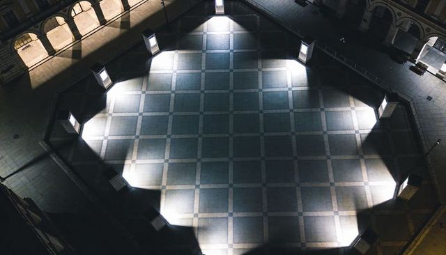 Symmetric star-shaped light pattern over central tiled plaza at night with lit columns