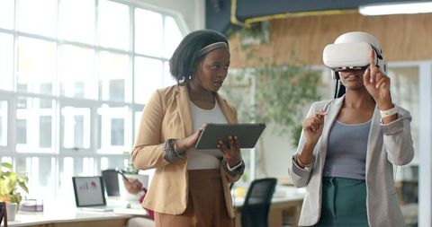 Businesswomen Testing Virtual Reality Headset in Modern Office Collaborating with Tablet