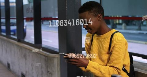 Young commuter tapping smartphone at bus shelter with digital data overlay
