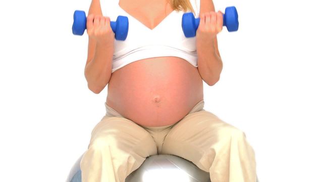 A pregnant woman sits on an exercise ball while lifting dumbbells for a prenatal fitness routine. Useful for maternity health guides, prenatal fitness programs, and wellness articles focusing on safe and effective exercises during pregnancy.