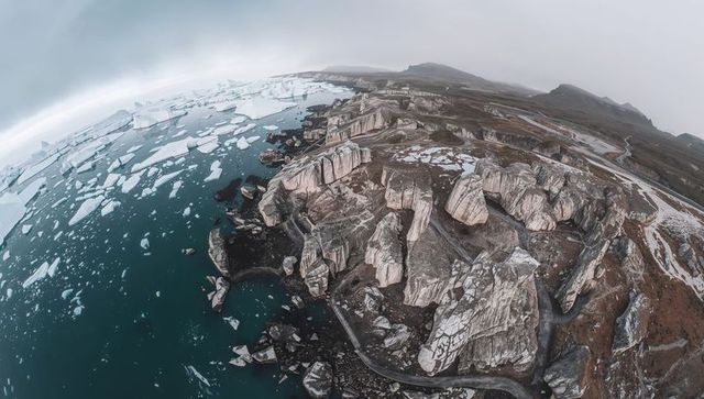 Aerial panorama of stratified coastal cliffs with winding road and drifting icebergs