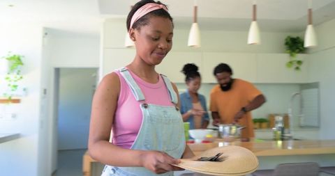African family cooking together in modern kitchen with teen holding straw hat and smiling