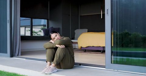 Woman sitting contemplatively by open sliding door