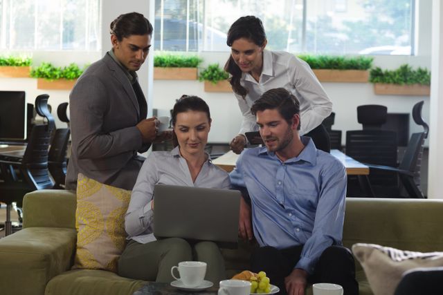 Group of executive professionals collaborating over a laptop in a modern office environment. Suitable for use in corporate websites, business presentations, and articles on teamwork and productivity.