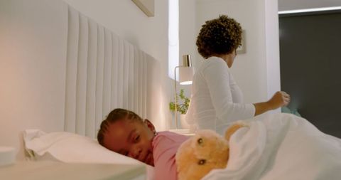 Mother Adjusting Lamp as Daughter Snuggles with Teddy in Bedroom