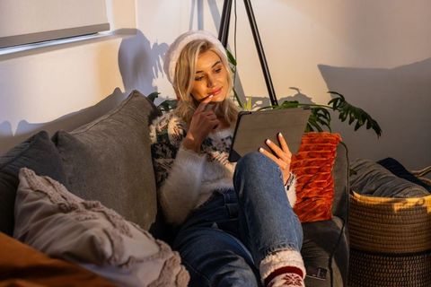 Cozy evening lounging on sofa reading tablet wearing fuzzy sweater and beanie