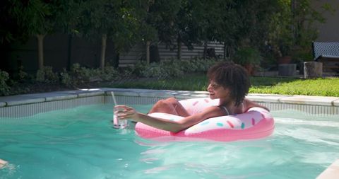 Woman Relaxing on Pink Donut Float in Home Pool Smiling