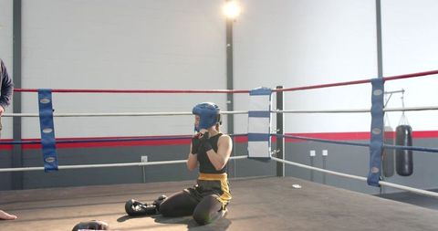 Male trainer watching female boxer kneeling in ring during sparring training session