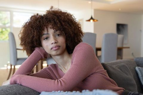 African american woman reclining on gray sofa in minimalist living room, relaxed portrait