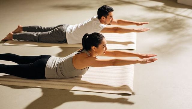 Man and woman practicing prone back extension on yoga mats in sunlit minimal studio