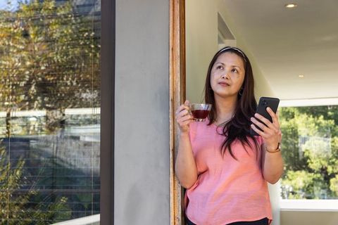 Asian Woman Enjoying Tea and Smartphone in Modern Home