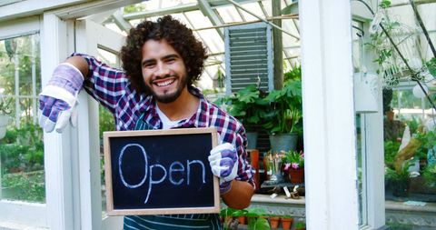Smiling man holding open sign in lush greenhouse